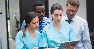 Medical team discussing over digital tablet in hospital corridor